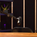 Podcastový mikrofón na ramene nad stolom v modernom štúdiu s policami a podsvietením.